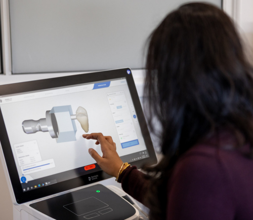 Person with dark hair uses a touchscreen monitor to view a 3D dental model